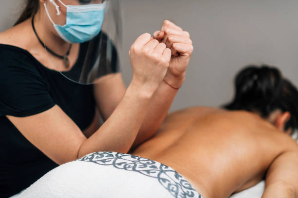 istock Lomilomi Practitioner wearing a Protective Mask, Giving Back Massage at a Wellness Center 1299054650