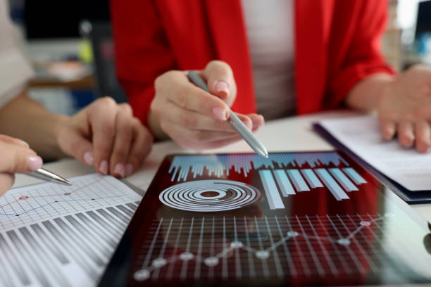 Business women studying charts and diagrams on digital tablet closeup stock photo