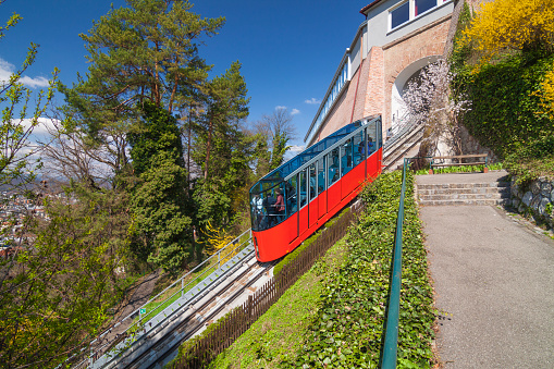 Austria - Graz - The bright red funicular (Schlossbergbahn) travels up to Schlossberg hill from the city center during warm spring day. It has gradient 60% and gives panoramic aerial view of the historic downtown