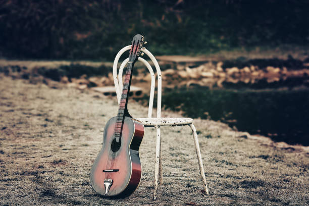 chitarra acustica sdraiata di fronte alla casa con sedia vuota - classical music music musical instrument brown foto e immagini stock