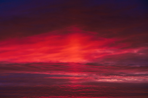 Beautiful colorful dramatic sky with clouds at sunset. Bright orange setting sun low on the horizon. Cirrus clouds change color from blue to yellow to red. Stunning backdrop, gorgeous scenery.