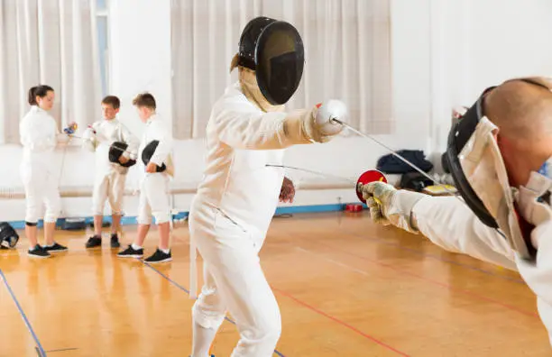 Adults and teens wearing a fencing uniform practicing with foil at the gym