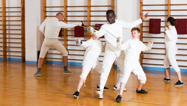 Coach demonstrating fencing movements to kids Trainer demonstrating to young athletes stances and movements with rapier during fencing workout in gym fencing sport stock pictures, royalty-free photos & images