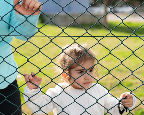 Portrait of mother and daughter seen behind chainlink fence. Mother is wearing a protective face mask. Shot in outdoor with a full frame mirrorless camera.