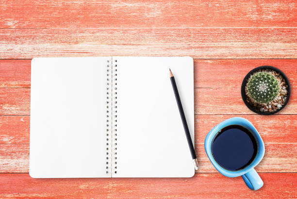 istock Blank paper notebook and black pencil with cup of coffee on wood table 1299062109