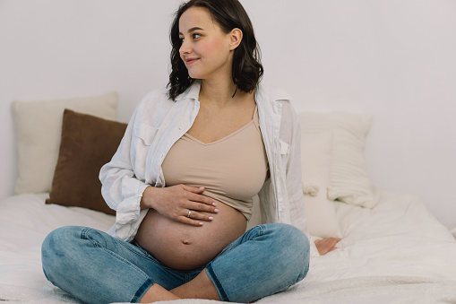 Attractive pregnant woman is sitting in bed and holding her belly. Last months of pregnancy. Pregnancy Concept.