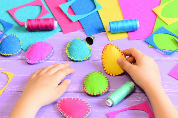 istock Child hold a felt Easter egg in his hand. Small child made colourful felt Easter crafts diy. Tools and materials for sewing handicraft on wooden table. Easy fun kids Easter crafts activities concept 1299065780