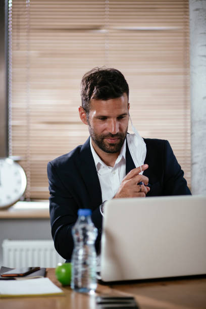 istock Young businessman with a mask working in his office on laptop. 1299065785