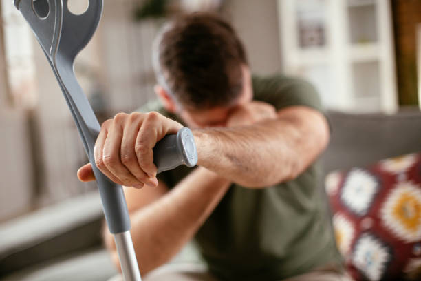 istock Young man with a hand on his crutches sitting on sofa 1299067742
