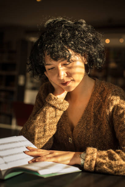 istock Young woman reading book in library. 1299069181