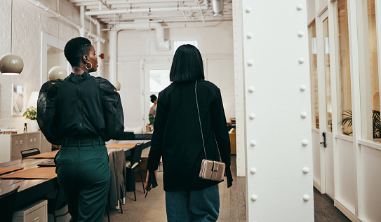 Rearview shot of two young businesswomen having a discussion while walking through a modern office