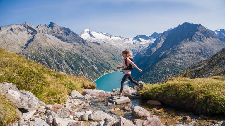 Young woman jumping over mountain stream in majestic landscape