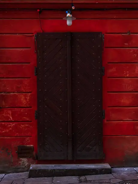 Vintage brown wooden door. Antique building exterior detail. Street photo. Retro wood boards. Empty abstract grunge painted texture, colorful vibrant red weathered wall.