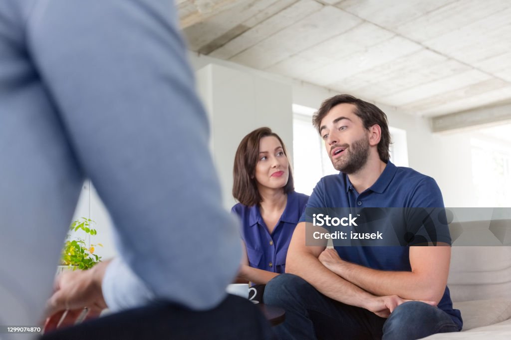 Couple discussing problems with psychotherapist Mid adult couple discussing problems with psychotherapist sitting in living room. They are in meeting at home. Couple - Relationship Stock Photo