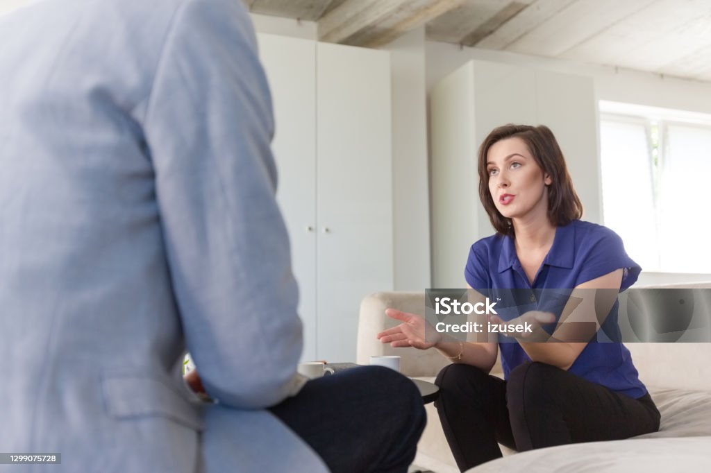 Woman discussing problems with psychotherapist Mid adult woman discussing problems with psychotherapist sitting in living room. They are in meeting at home. Mental Health Professional Stock Photo