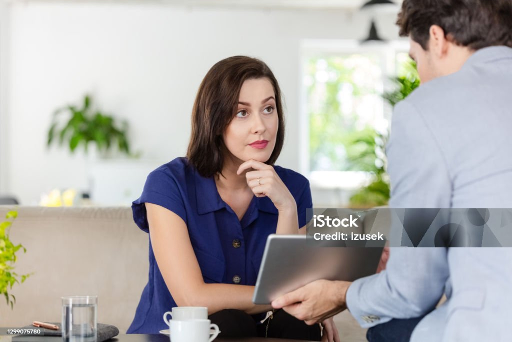 Woman talking with financial advisor at home Cheerful mid adult woman having meeting with financial advisor or insurance agent at home, sitting on sofa in living room. Financial Advisor Stock Photo
