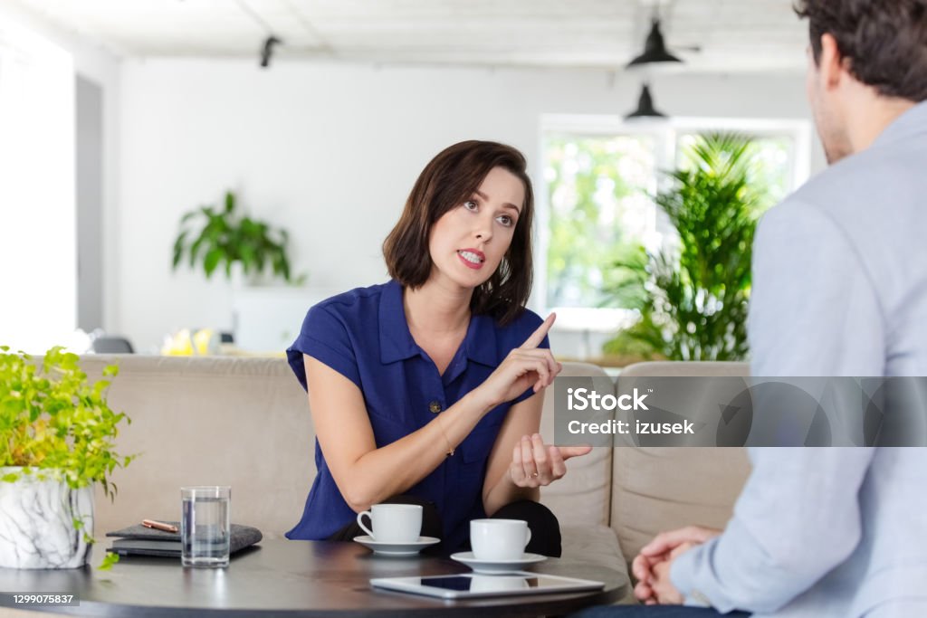 Woman talking with insurance agent at home Mid adult woman discussing with financial advisor or insurance agent at home, sitting on sofa in living room. Uncertainty Stock Photo