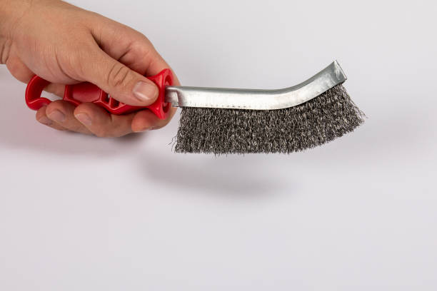 Metal wire brush with red plastic handle in a man's hand. White background.