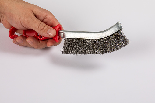 Metal wire brush with red plastic handle in a man's hand. White background.