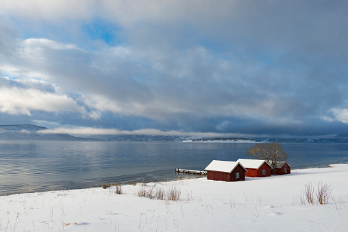 Norwegian sheds on the shore of a Fjord in Northern Norway in winter. Clouds over the Malangen fjord are bringing in new snow.