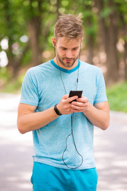 athlète d’homme sur le visage occupé installant le traqueur de forme physique avec l’application de smartphone, fond de nature. entraînement sportif avec gadget podomètre. athlète avec le traqueur de forme physique ou le podomètre. concept de gad - natural bristle audio photos et images de collection