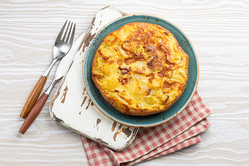 Homemade Spanish tortilla - omelette with potatoes on plate on white wooden rustic background top view. Traditional dish of Spain Tortilla de patatas for lunch or snack, overhead