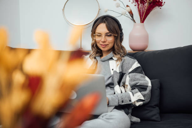 istock Beautiful young woman using laptop, sitting on couch at home. 1299080122
