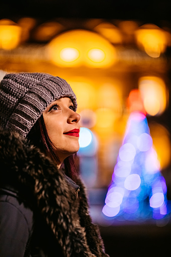 Portrait of young beautiful woman outdoors at night at Christmas time in warm clothes.