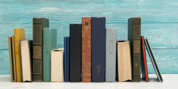 istock Stack of books on bookshelf in Library. Back to School education concept on colored blue background. Open hardback book on wooden desk table. 1299083738