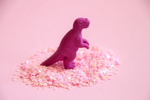 Dinosaur figure standing in pink glitters. Pink party tyrannosaur