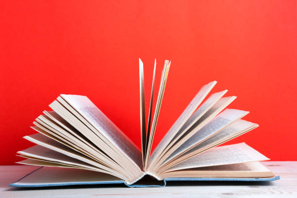 istock Book on bookshelf in Library. Back to School education concept on red background. Open hardback book on wooden desk table. 1299084908