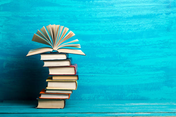 istock Stack of books on bookshelf in Library. Back to School education concept on colored blue background. Open hardback book on wooden desk table. 1299085484