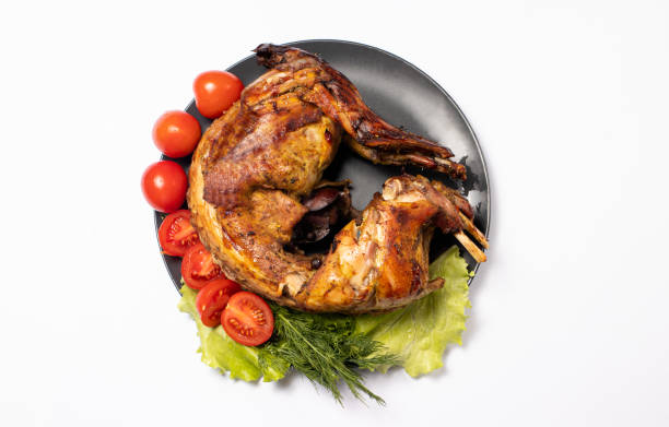 istock Rabbit meat baked with vegetables and herbs on a plate on a white background. With tomatoes and lettuce, top view 1299087880