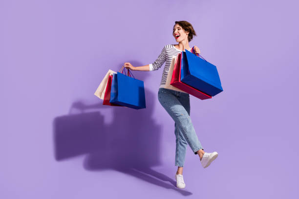 foto de longitud completa de adorable joven vestida ropa casual bailando sosteniendo coloridas gangas de fondo de color púrpura aislado - women bag fotografías e imágenes de stock