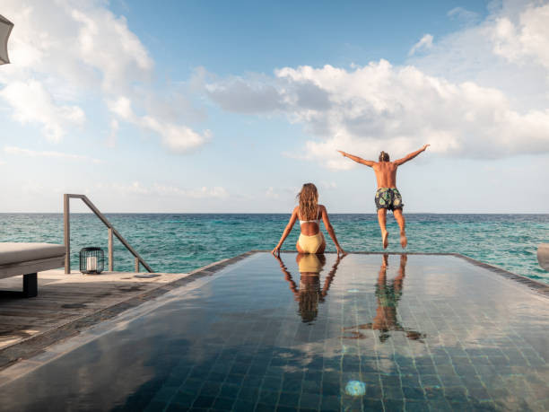 豪華な休暇を楽しむカップル、プールから海にジャンプする男 - vacations infinity pool relaxation swimming pool ストックフォトと画像