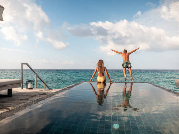 casal curtindo férias luxuosas, homem pulando de piscina para mar - vacations infinity pool relaxation swimming pool - fotografias e filmes do acervo