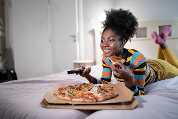 istock Young woman rests after work, eating pizza and watching TV 1299092422