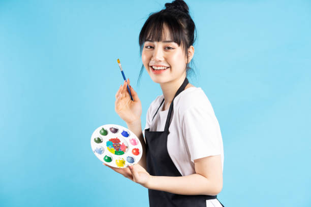 Artist Beautiful Asian female painter holding quill pen and color palette on blue background painter artist stock pictures, royalty-free photos & images