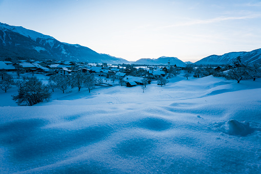 Snow covered alpine winter landscape during blue hour dusk with view over small Austrian traditional village in Wildermieming, Tirol, Austria