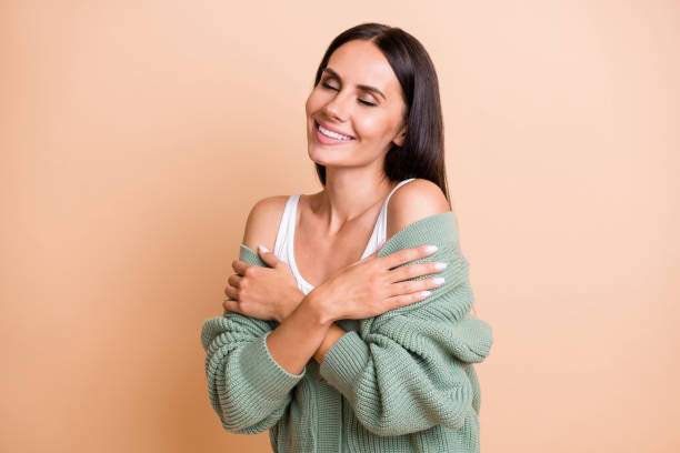 Photo of dreamy happy woman stand empty space touch shoulders closed eyes isolated on pastel beige color background Photo of dreamy happy woman stand empty space touch shoulders closed eyes isolated on pastel beige color background. cardigan sweater stock pictures, royalty-free photos & images