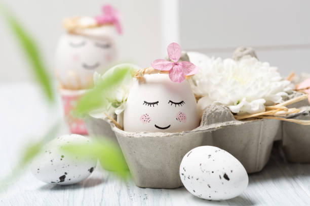 istock Easter holiday concept with cute handmade white eggs, tree branches, quail feathers and spring flowers on white wooden background. 1299095456