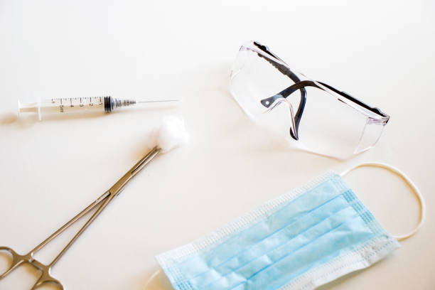 Needle, face masks and safety glasses on the white background, sterile protection