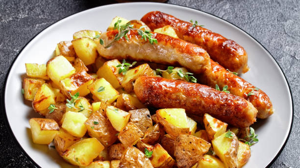 istock sausages and roasted potatoes on a  plate with golden fork and knife 1299098562
