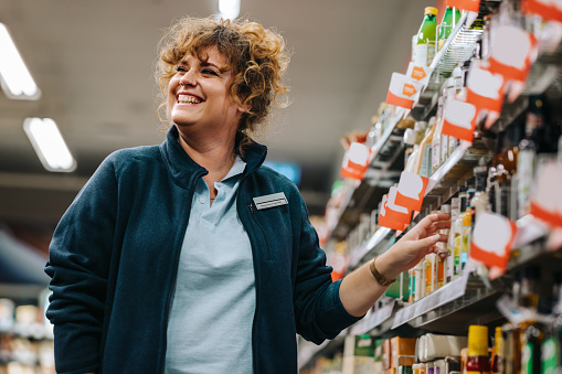 Confident businesswoman standing by the shelves and smiling in supermarket. Female manager at a grocery store.