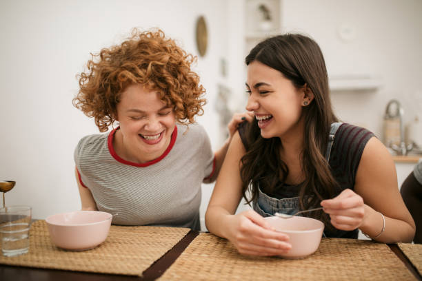 Two Caucasian female having a meal at home Two happy Caucasian female friends enjoying their meal in the kitchen, talking, smiling and bonding college dorm party stock pictures, royalty-free photos & images