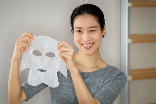 Female youtuber introducing cosmetic product and wearing facial mask in front of camera