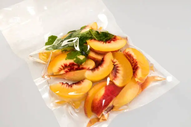 peach slices with mint leaves vacuum packed sealed for sous vide cooking on gray background
