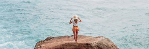 Young woman on rock above sea contemplating the beautiful view enjoying nature and outdoors. Tropical climate, people travel Sri Lanka