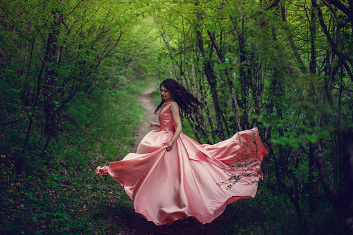 River witch, sitting on a rock in river. Pink long dress, a fabulous image.Fashionable toning. Creative color. Beautiful dancer in a mystical forest by the river