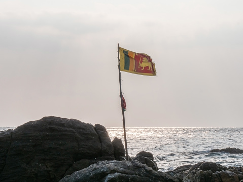 Sea view with Sri Lanka flag on rock at sunset, dramatic sky. Travel no people